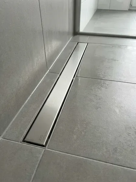 תעלת ניקוז ג׳ורדן מותקנת במקלחת מודרנית עם ריצוף אפור